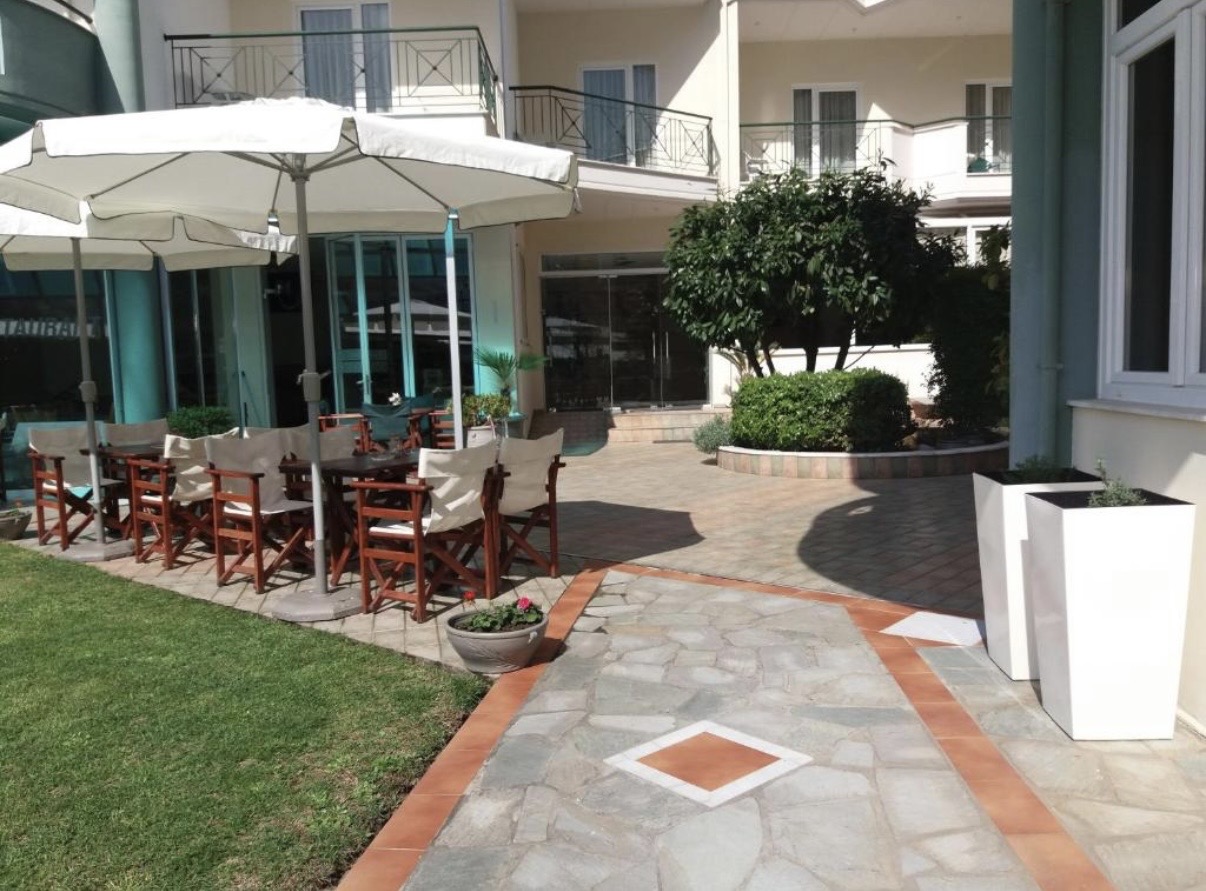 Sunny garden terrace with dining tables and white umbrellas at Hotel Filoxenia Beach